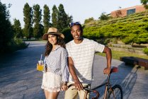 Pareja con bebidas y bicicleta posando sobre parque urbano - foto de stock