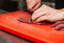 Крупним планом вид чоловічих рук, що нарізають м'ясо на червону пластикову дошку — стокове фото