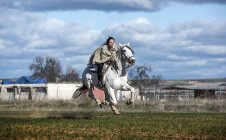 Vue latérale de la femme à cheval galopant rapidement dans un champ rural — Photo de stock