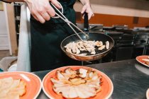 Середина кухаря розміщує інгредієнти з щипцями на тарілках на кухні ресторану — стокове фото