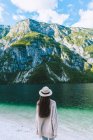 Chica en sombrero de pie en la orilla del lago - foto de stock