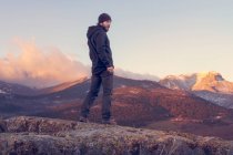 Homme au sommet de la montagne debout sur le rocher regardant un beau lever de soleil dans la montagne enneigée ensoleillée — Photo de stock