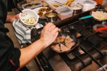 Vista ad alto angolo di chef aggiungendo ingredienti sulla padella a stufa — Foto stock