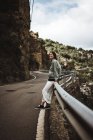 Весела жінка спирається на дорожній паркан в горах — стокове фото