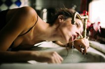Thirsty woman in lingerie drinking water from vintage tap in daylight — Stock Photo