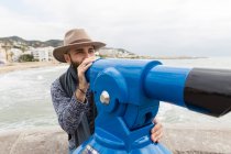 Homem barbudo em pé na costa e apontando com sightseeing máquina binocular — Fotografia de Stock