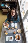 Висока кут портрет брюнетка жінка в окулярів, сидячи за столом сніданок і дивлячись на камеру — стокове фото