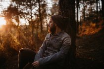 Uomo seduto nella foresta al tramonto e guardando da parte — Foto stock
