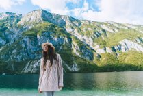 Girl in hat posing at mountain lake shore — Stock Photo