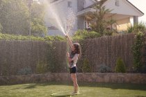 Side view of girl playing with hose at backyard on hot summer day — Stock Photo