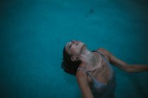 Portrait de femme en débardeur humide pliant le cou en arrière dans la piscine — Photo de stock