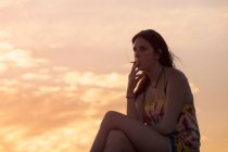 Young woman smoking a cigarette watching the sunset — Stock Photo