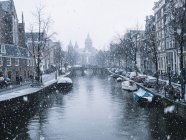 Canal de Amsterdã com fileiras de barcos ancorados em dia nevado — Fotografia de Stock