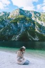 Girl in hat sitting lake shore — Stock Photo