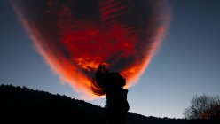 Menina silhueta contra nuvem vermelha no céu azul — Fotografia de Stock