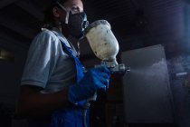 Low angle portrait of female mechanic wearing respirator using spray pistol — Stock Photo