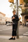 Retrato de comprimento total do menino inclinado no poste do semáforo na rua e olhando para o lado — Fotografia de Stock