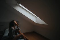 Brünettes Mädchen sitzt auf Bett gegen Dachbodenfenster — Stockfoto