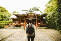 Back view of man with backpack standing at Asian style temple. — Stock Photo