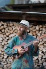 Uomo barbuto giocare ukulele su tronchi accatastati — Foto stock