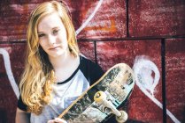 Femme blonde skateboarder posant avec skateboard au mur de graffiti — Photo de stock