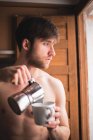 Спящий мужчина без рубашки наливает кофе в кружку и смотрит в окно . — стоковое фото