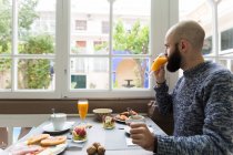 Horizontal en interiores disparo de hombre tomando jugo de naranja fresco desayunando en la cafetería . - foto de stock