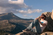 Jeune homme détendu bronzant au sommet de la montagne au coucher du soleil — Photo de stock