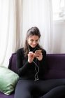 Sorridente donna bruna in auricolare seduta sul divano e smartphone di navigazione — Foto stock