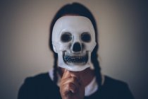 Portrait of unrecognizable girl in black dress holding skull mask in front of face. — Stock Photo