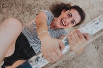 Laughing girl looking at camera while hanging on wooden bar — Stock Photo