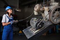 Female mechanic operating hoist to lift compressor engine — Stock Photo