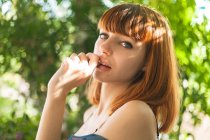 Portrait of redhead girl posing with thumb at lips and looking at camera — Stock Photo