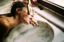 Brunette woman in lingerie drinking water from vintage tap in daylight — Stock Photo