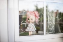 Vista de cerca de la muñeca moderna de pelo rosa de pie detrás de la ventana - foto de stock