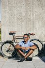 Человек в солнечных очках сидит рядом с велосипедом — стоковое фото