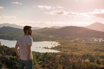 Молодий чоловік дивиться захід сонця на озері з вершини пагорба — стокове фото