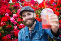 Portrait of cheerful bearded man looking at camera and proposing  toast with smoothie glass. — Stock Photo