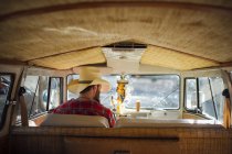 Rear view of man in cowboy hat sitting at drivers seat of retro van and looking aside — Stock Photo
