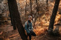 Чоловік спирається на дерево в лісі і дивиться в сторону — стокове фото