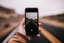 Cortar mão segurando smartphone e tiro cena da estrada — Fotografia de Stock
