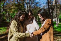 Portrait of three young women chatting and smiling outside in the park — Stock Photo