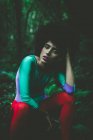 Menina sensual com cabelo encaracolado sentado na floresta e olhando para a câmera — Fotografia de Stock