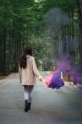 Girl walking with smoke torch at forest road — Stock Photo