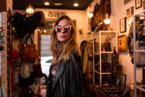 Young girl in sunglasses posing on background of clothing room. — Stock Photo