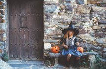 Menina em traje de bruxa sentado no banco — Fotografia de Stock