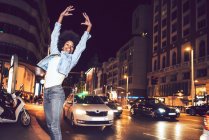 Beautiful young black woman jumping in street at night — Stock Photo