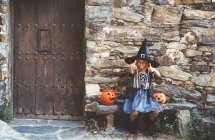Girl in witch costume sitting on bench — Stock Photo