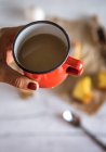 Above of hand holding red mug of hot chocolate over table with bakery — Stock Photo