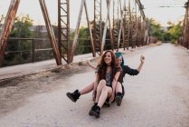 Meninas sentadas no skate e ridding na ponte — Fotografia de Stock